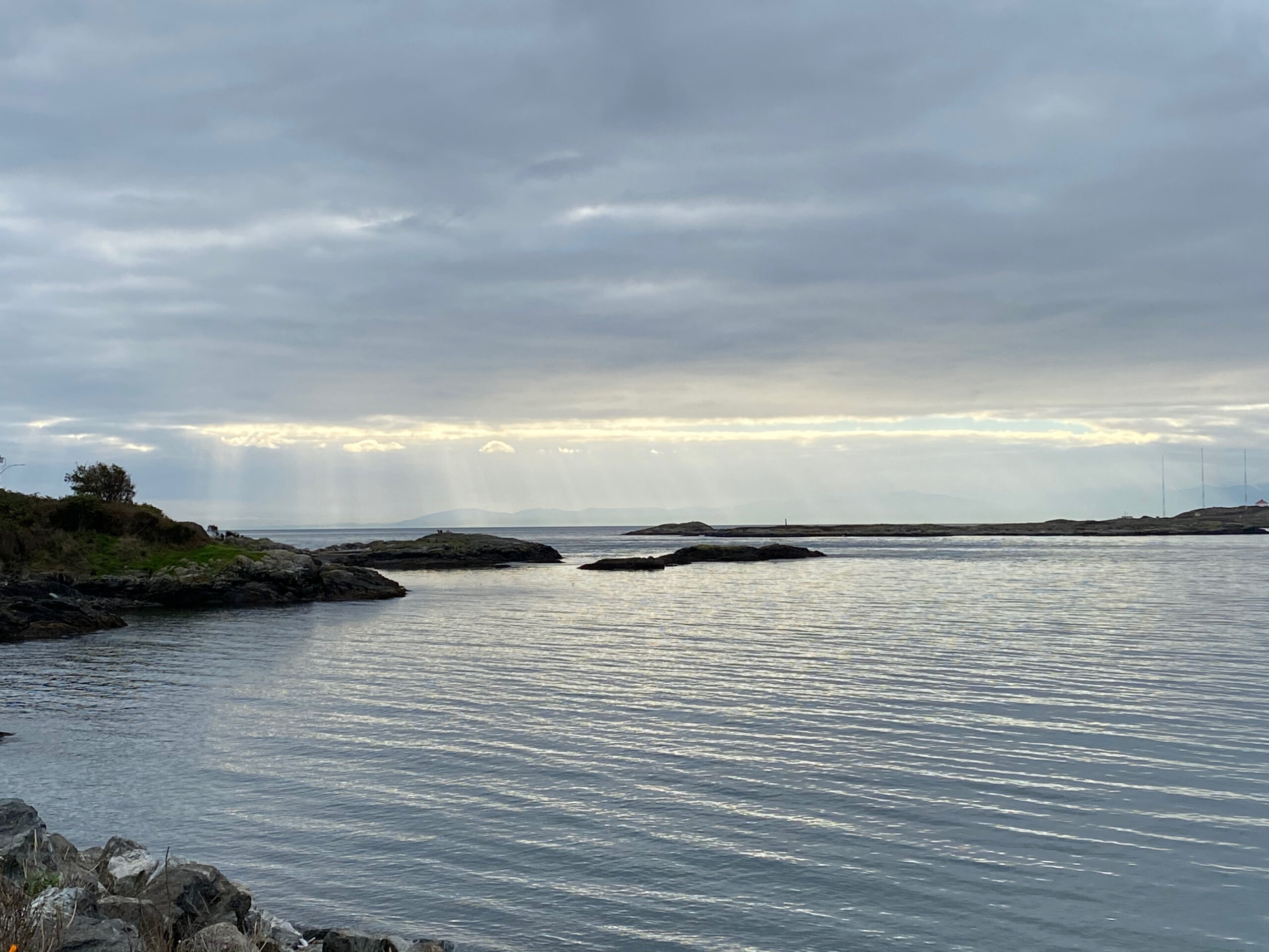 a calm ocean bay with a strip of sunlight sending rays down to the water in the distance 