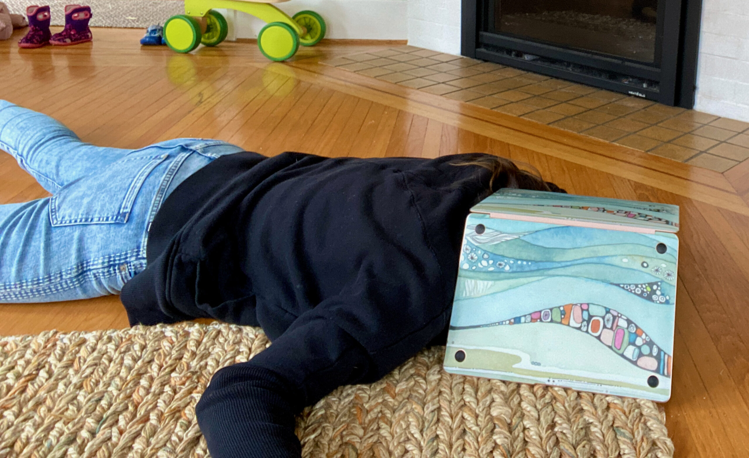 a woman lays on the floor, exhausted, with a laptop over her head.